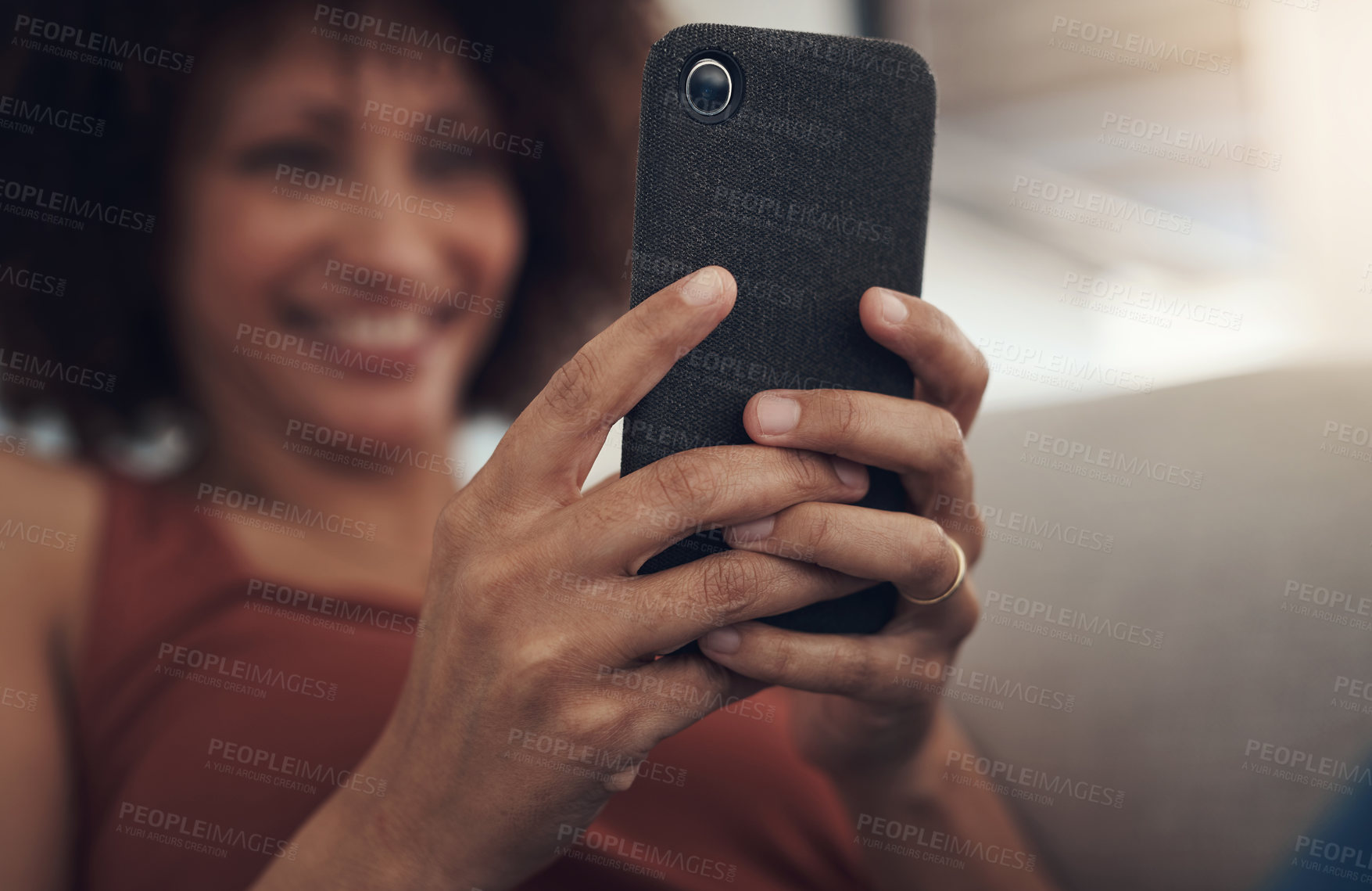 Buy stock photo Defocused of a young woman sitting on her sofa in the living room at home and using her cellphone