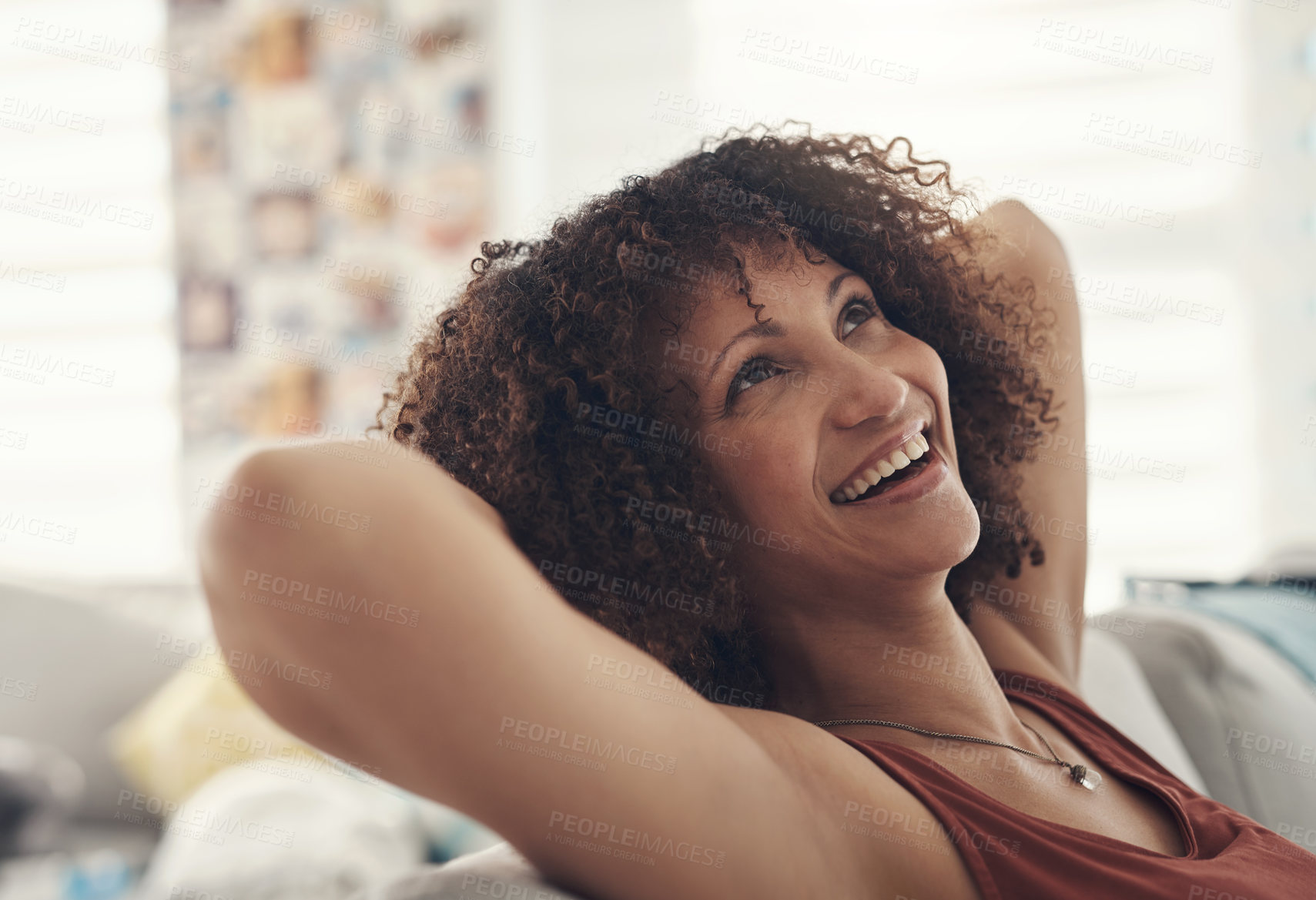 Buy stock photo Shot of an attractive young woman sitting on her sofa in her living room with her arms behind her head