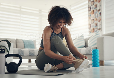Buy stock photo Shot of an attractive young woman sitting alone in her living room and tying her shoelaces before working out