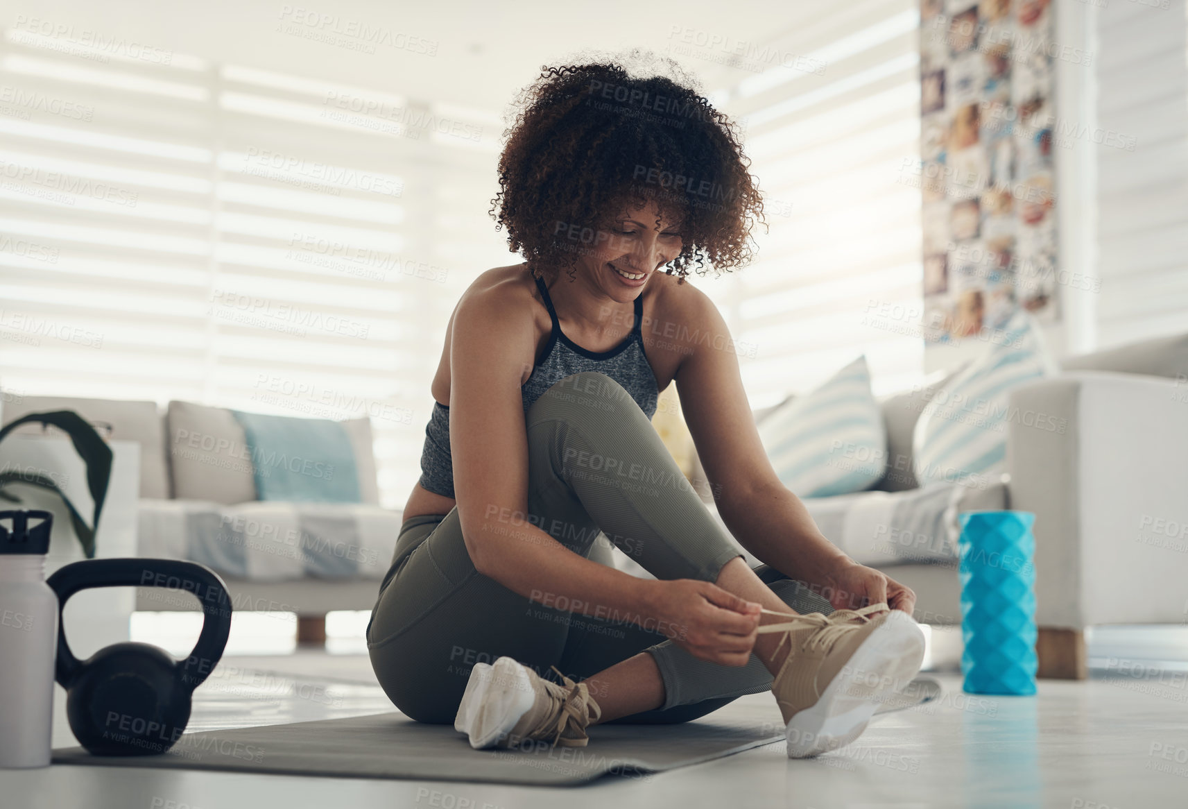 Buy stock photo Shot of an attractive young woman sitting alone in her living room and tying her shoelaces before working out