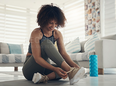Buy stock photo Shot of an attractive young woman sitting alone in her living room and tying her shoelaces before working out