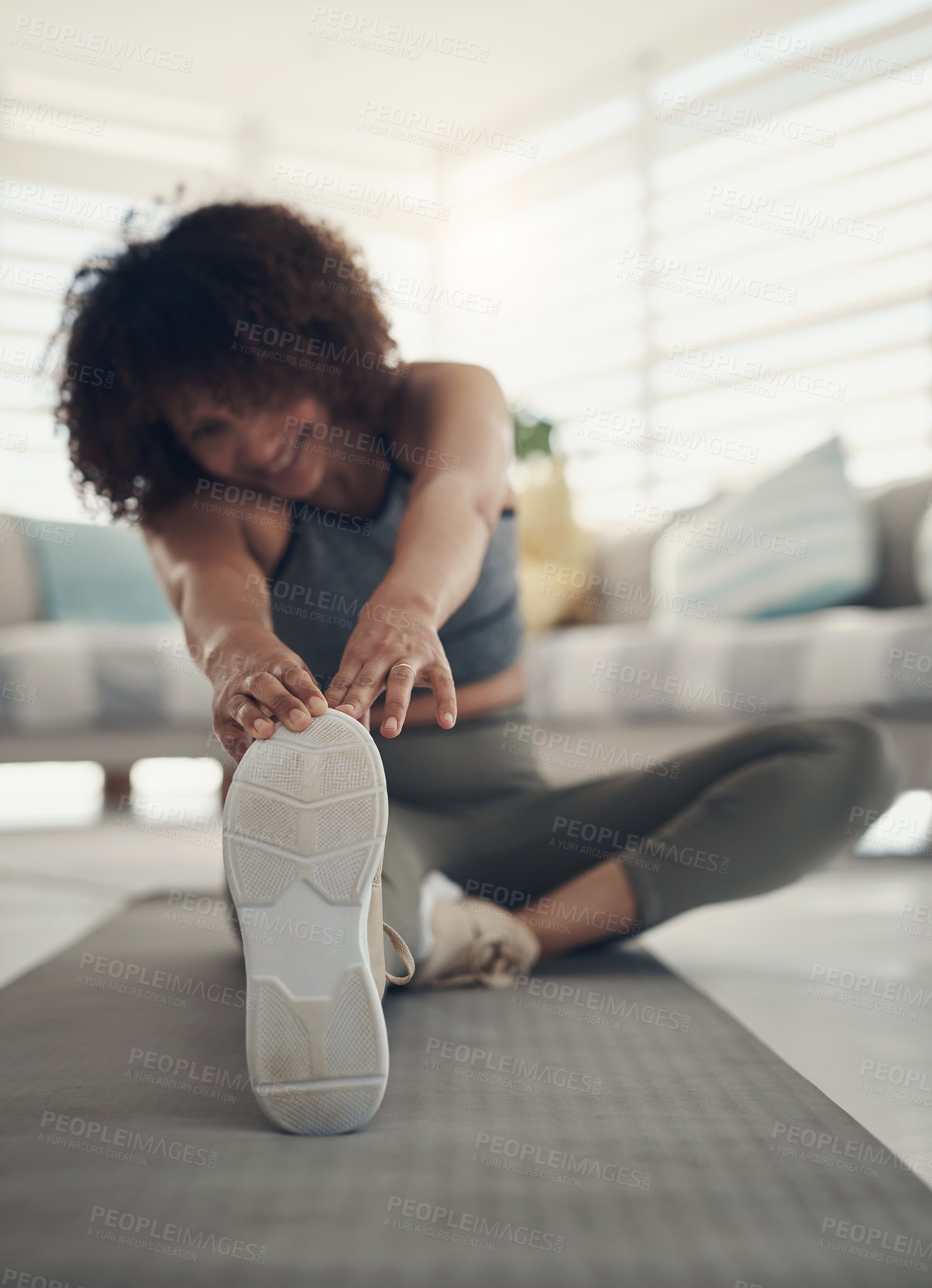 Buy stock photo Defocused shot of a young woman sitting alone in her living room and stretching before working out