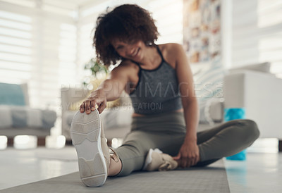 Buy stock photo Defocused shot of a young woman sitting alone in her living room and stretching before working out
