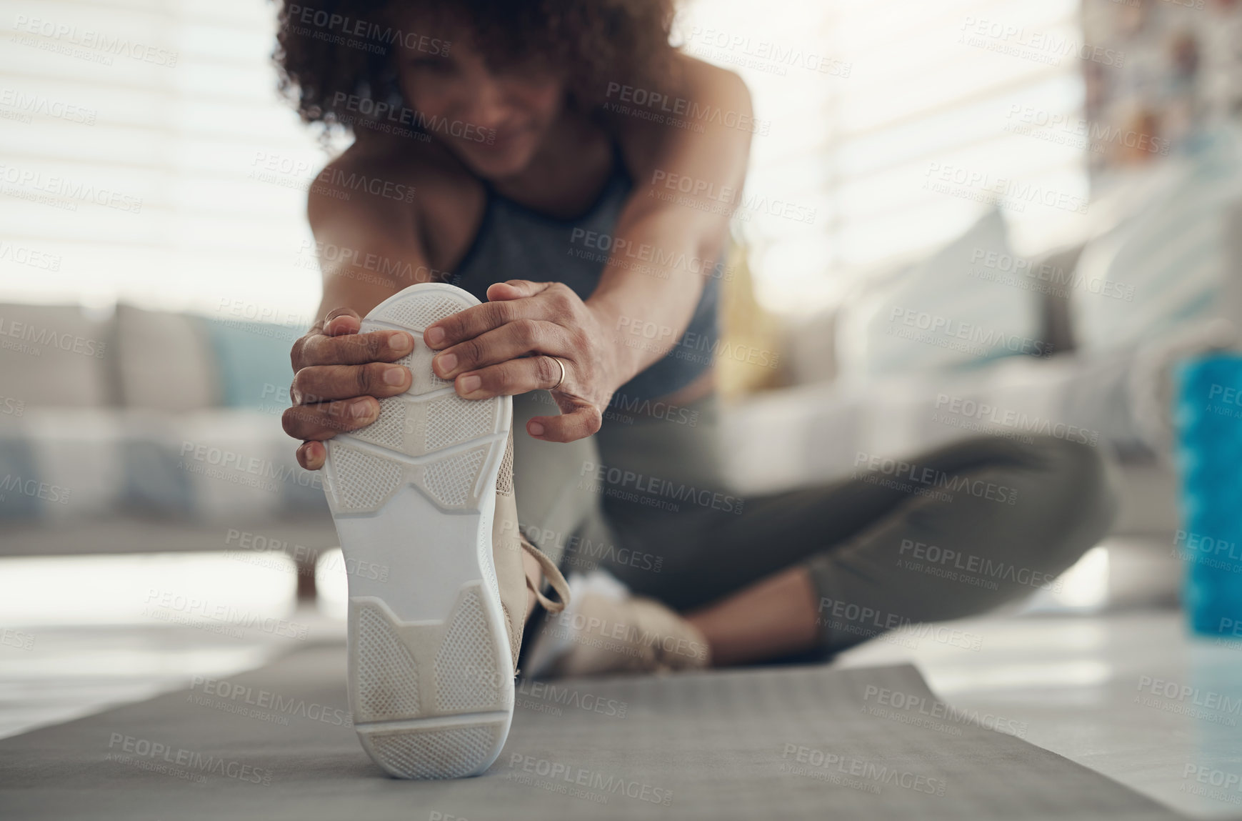 Buy stock photo Defocused shot of a young woman sitting alone in her living room and stretching before working out