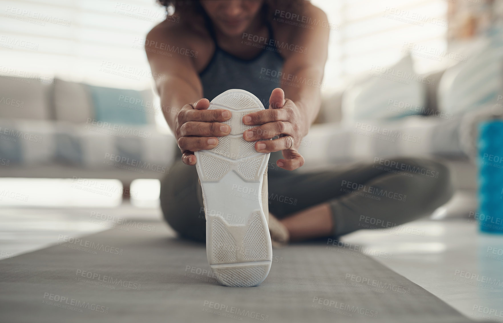 Buy stock photo Cropped shot of an unrecognizable woman sitting alone in her living room and stretching before working out