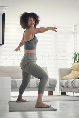 Buy stock photo Full length shot of an attractive young woman practising yoga in her living room at home and holding a warrior pose