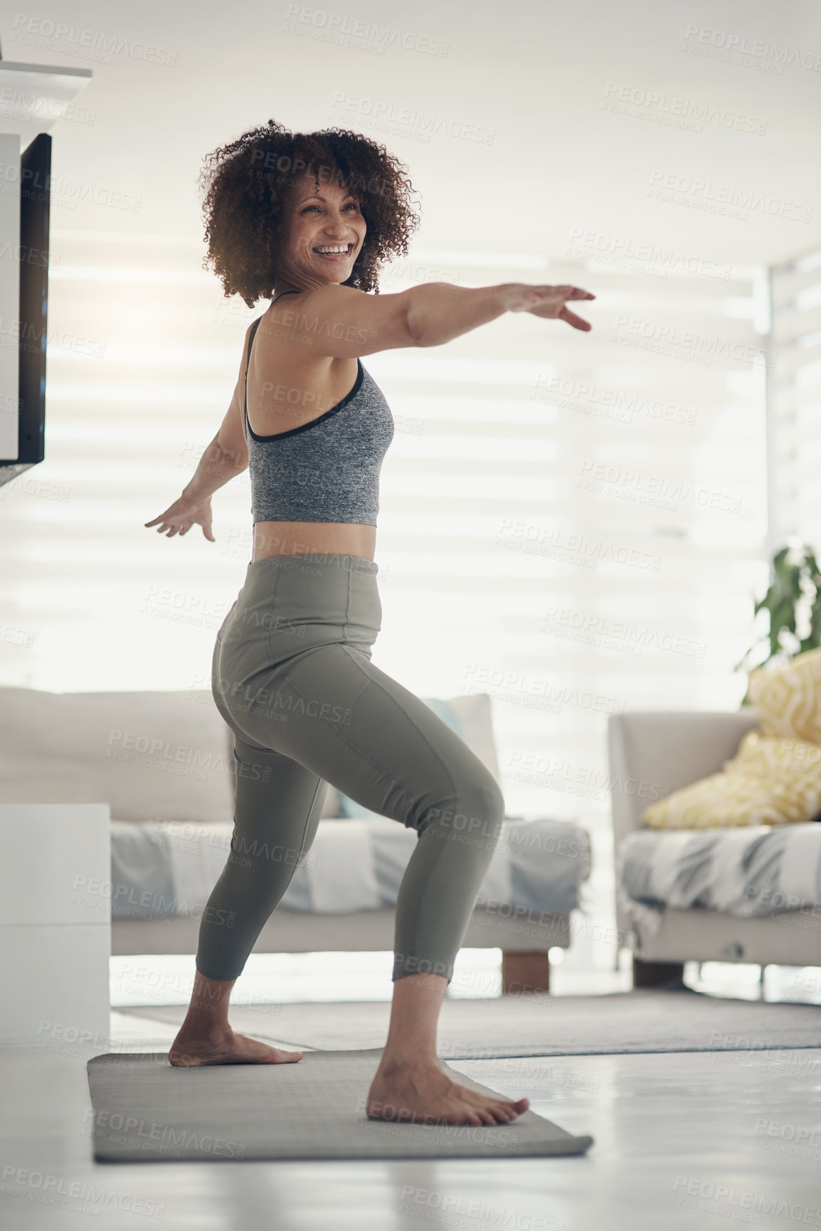 Buy stock photo Full length shot of an attractive young woman practising yoga in her living room at home and holding a warrior pose