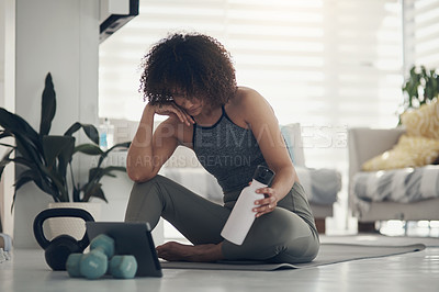 Buy stock photo Shot of an attractive young woman sitting in her living room and watching an online workout routine on a digital tablet