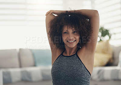 Buy stock photo Shot of an attractive young woman sitting alone in her living room and stretching before working out