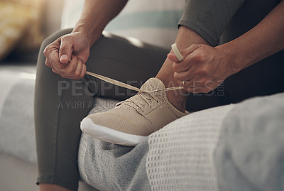Buy stock photo Cropped shot of an unrecognizable woman sitting alone on her sofa at home and tying her shoelaces before working out