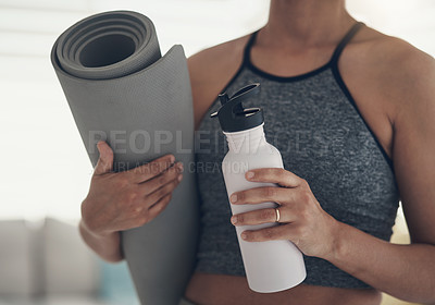 Buy stock photo Cropped shot of an unrecognizable woman standing alone at home and holding a yoga mat and a bottle of water
