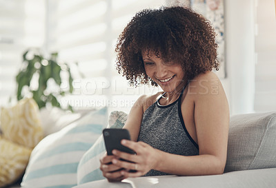 Buy stock photo Shot of an attractive young woman sitting alone on her sofa at home and using her cellphone