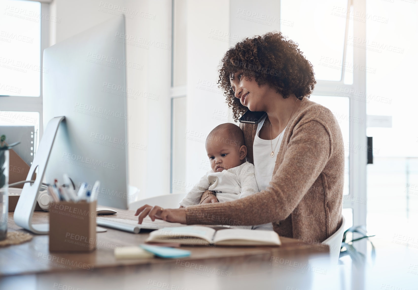 Buy stock photo Shot of a young woman using a smartphone and computer while caring for her adorable baby girl at home