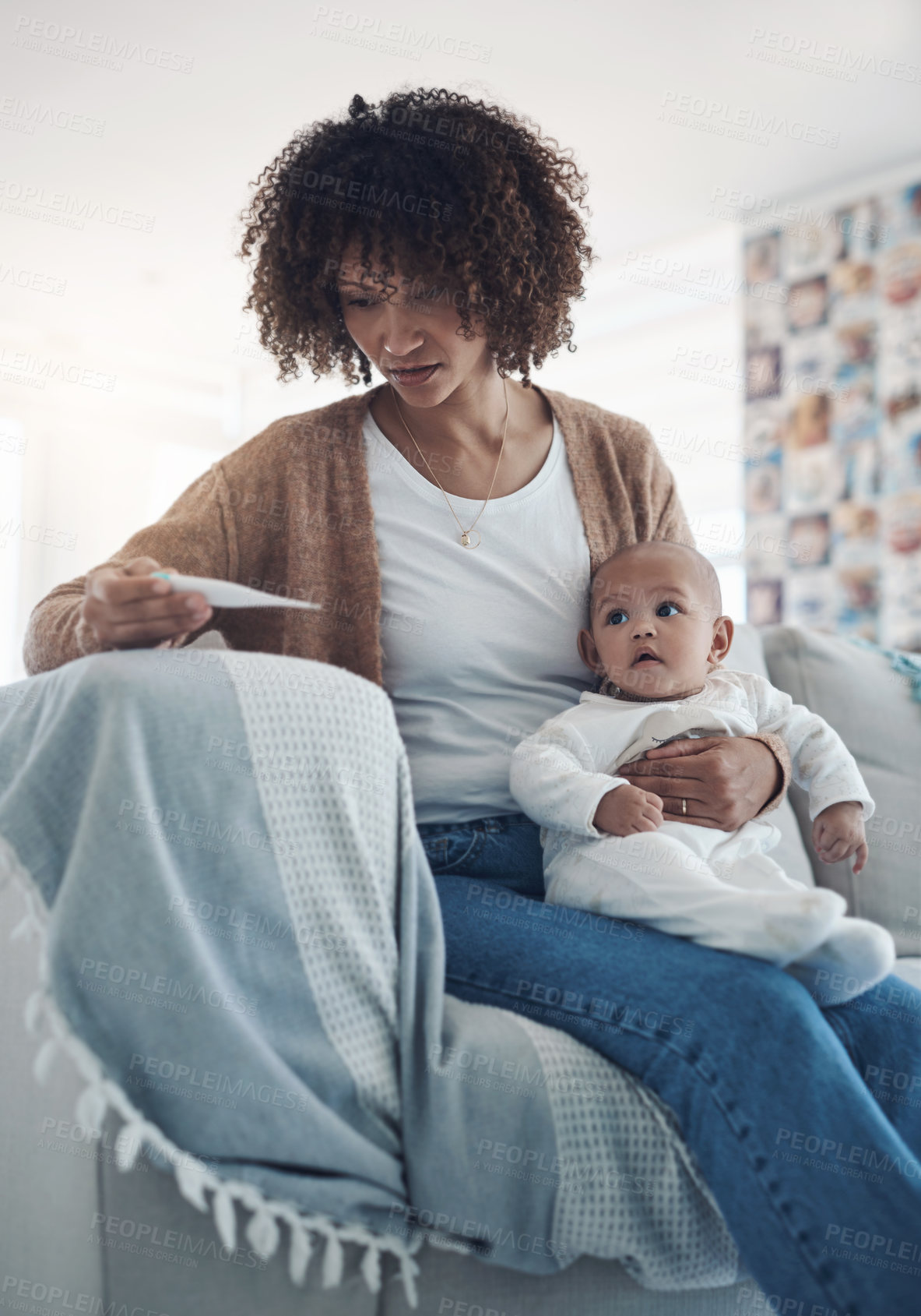 Buy stock photo Shot of a young woman checking her baby’s temperature with a thermometer on the sofa at home