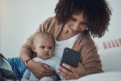 Buy stock photo Shot of a young woman using a smartphone while relaxing on the bed with her adorable baby girl at home