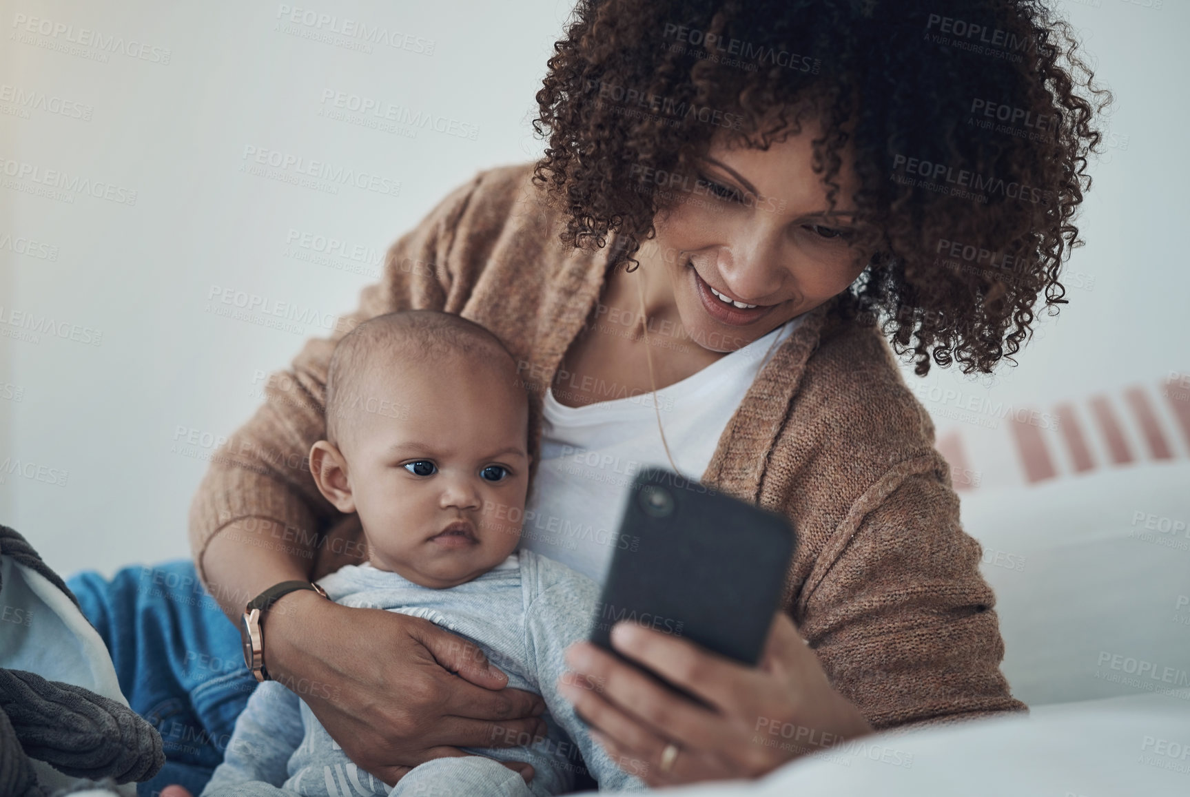 Buy stock photo Shot of a young woman using a smartphone while relaxing on the bed with her adorable baby girl at home