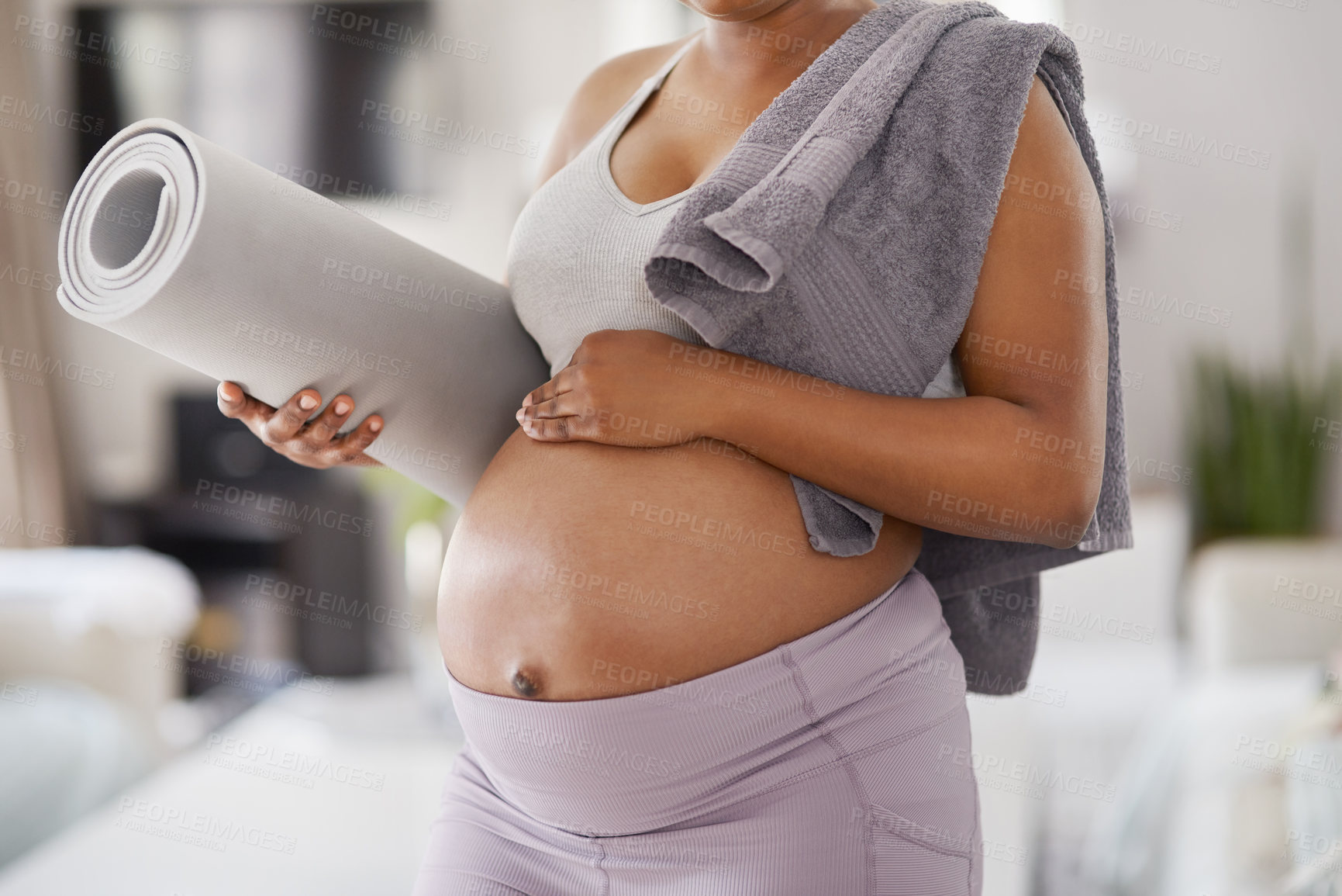 Buy stock photo Cropped shot of a pregnant woman posing with a yoga mat and a towel over her shoulder at home