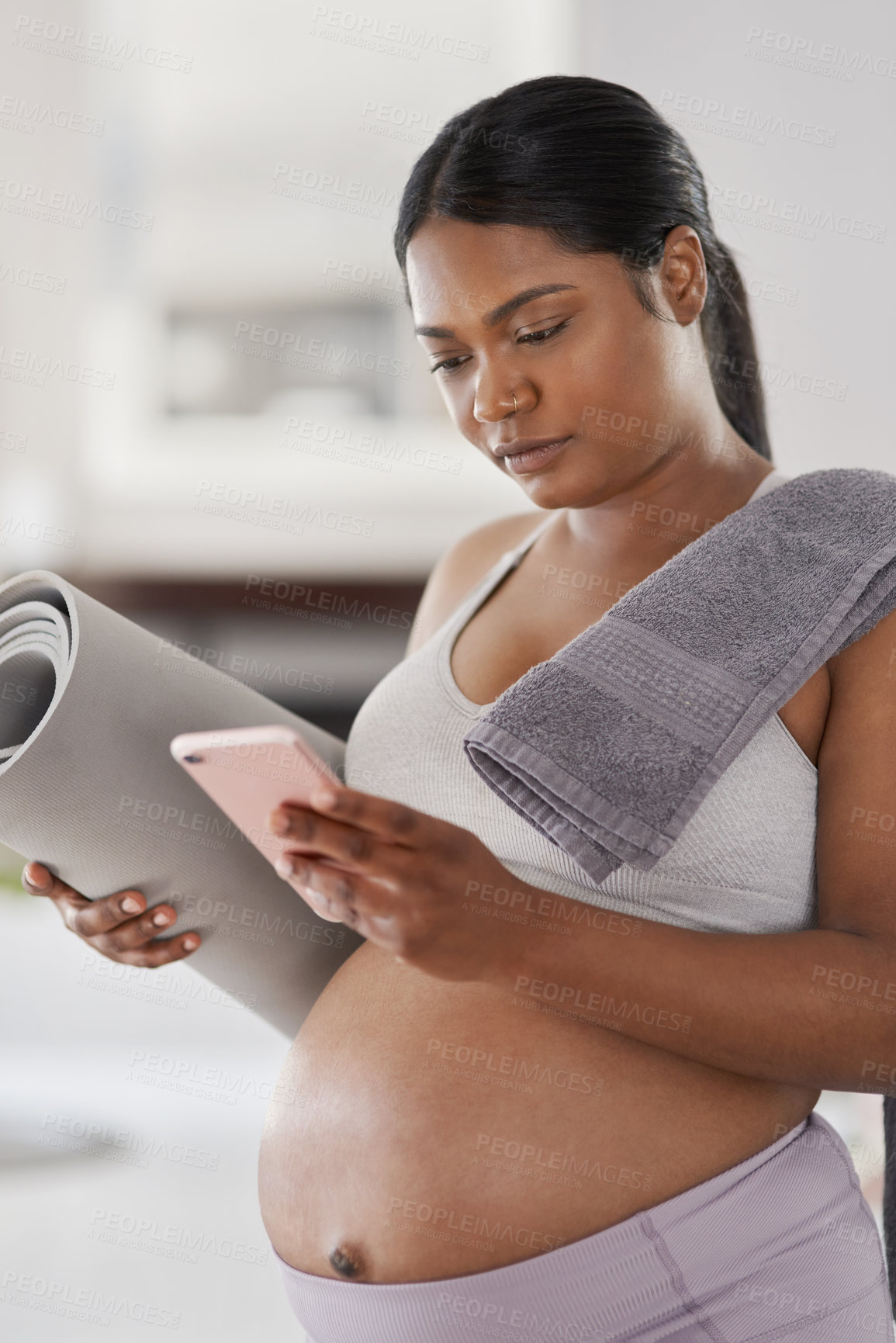 Buy stock photo Shot of a pregnant woman using her cellphone while holding her yoga mat home