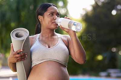 Buy stock photo Shot of a pregnant woman holding her yoga mat and drinking water while standing outside