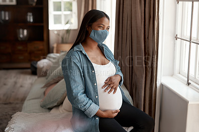 Buy stock photo Shot of a pregnant woman wearing a face mask and looking thoughtful at home