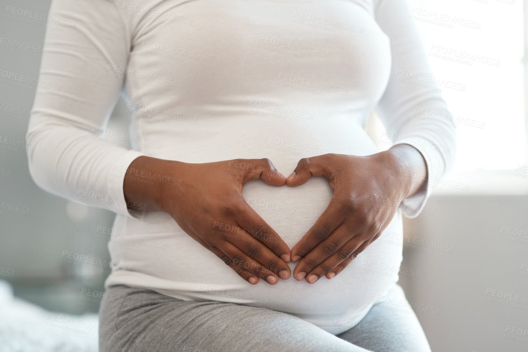 Buy stock photo Closeup shot of an unrecognisable woman making a heart shape with her hands on her pregnant belly at home