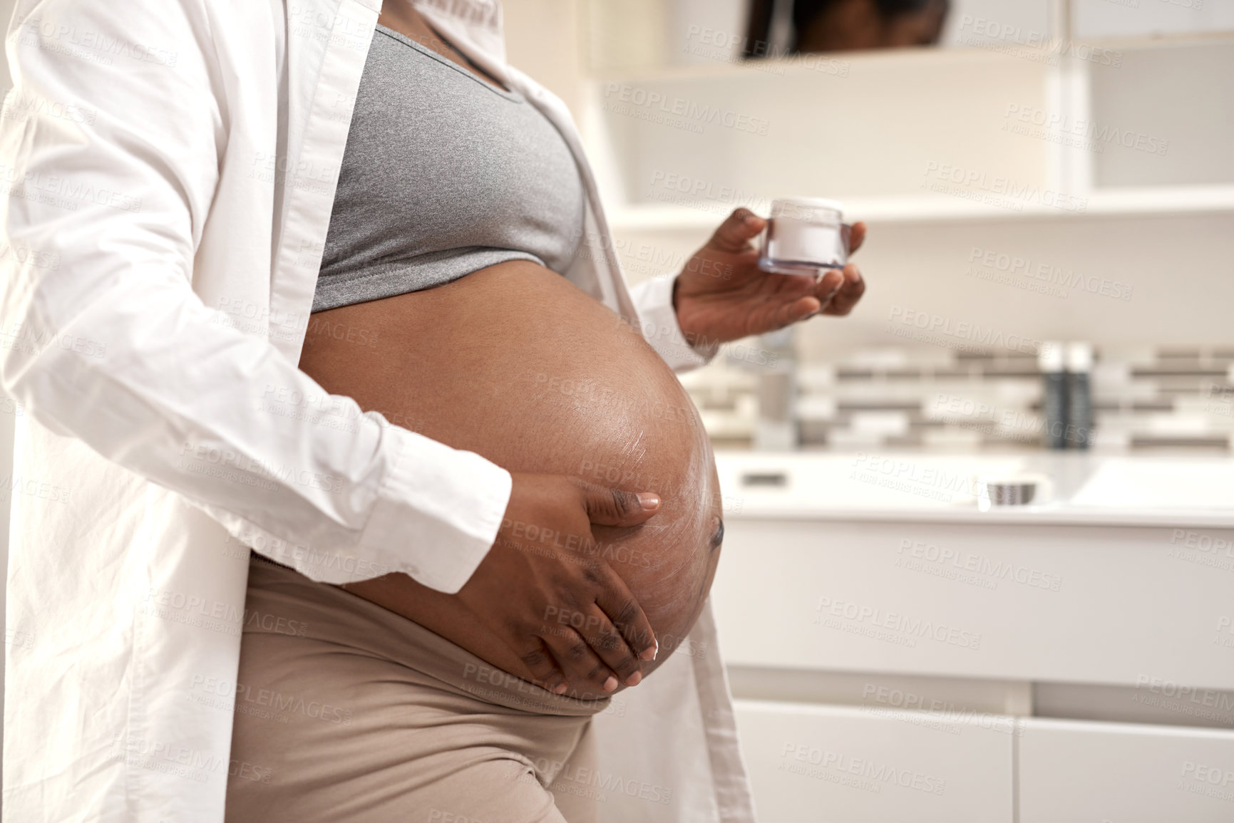 Buy stock photo Closeup shot of a pregnant woman applying cream on her stomach at home