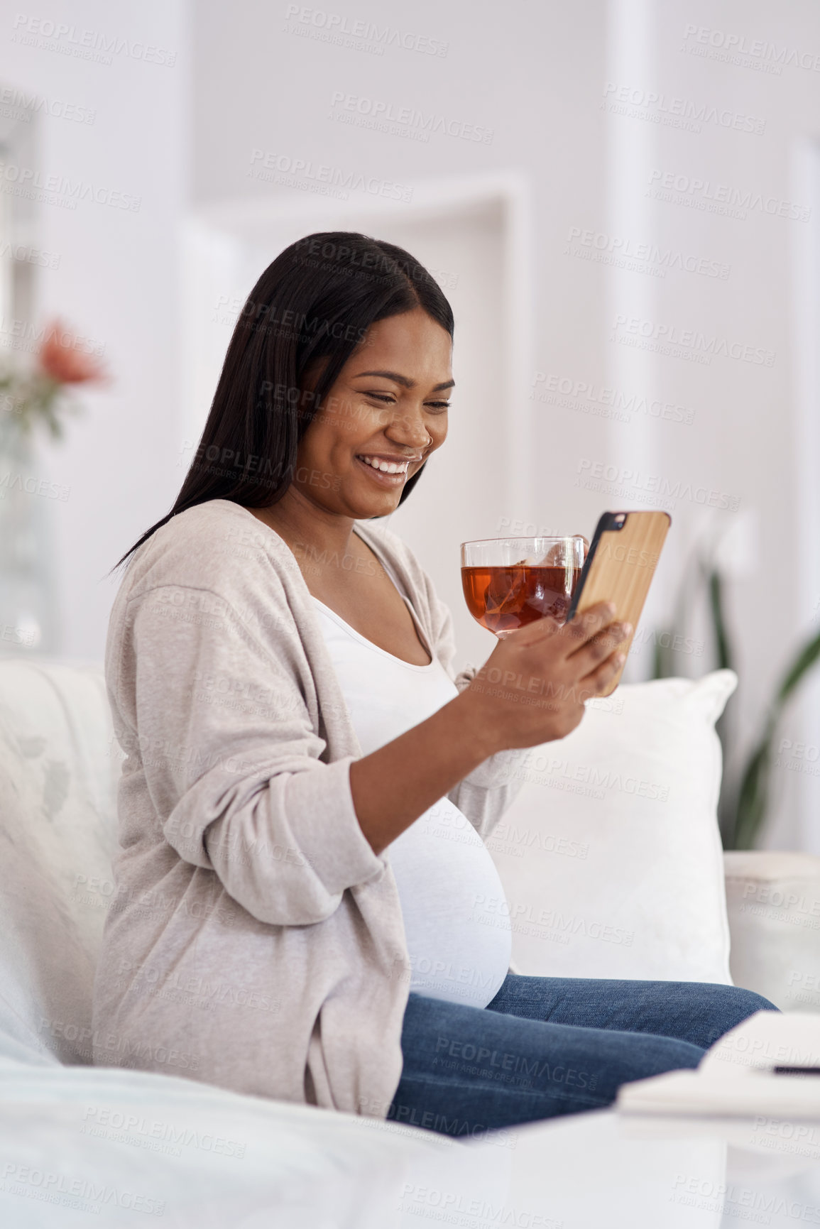 Buy stock photo Shot of a pregnant woman drinking tea and using her cellphone while sitting at home