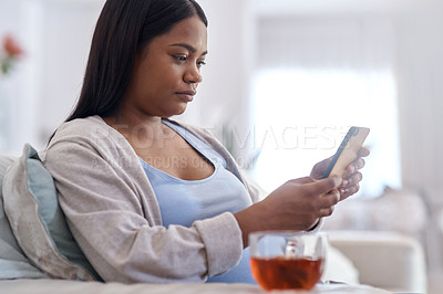 Buy stock photo Shot of a woman using her cellphone while sitting at home