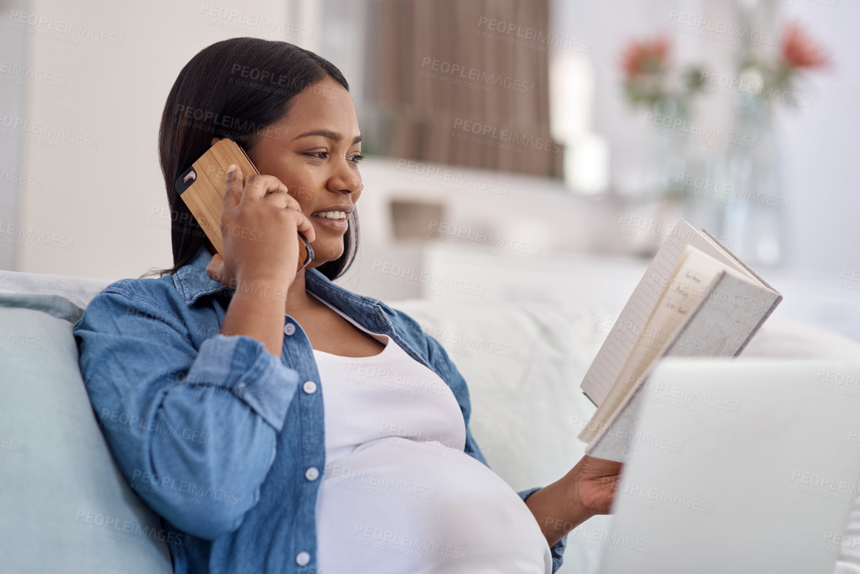 Buy stock photo Shot of a woman looking at her notebook while talking on her cellphone at home