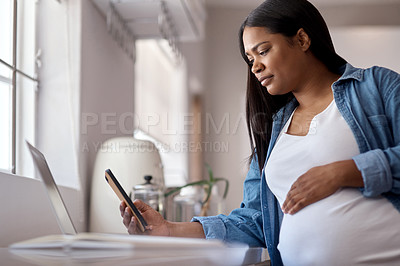 Buy stock photo Shot of a pregnant woman using her cellphone while sitting at home with her laptop