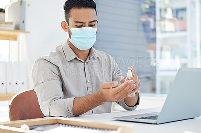 Buy stock photo Shot of a young man using hand sanitiser and wearing a mask at work in a modern office