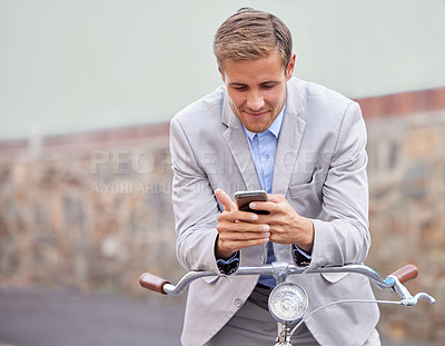 Buy stock photo Shot of a young businessman using his smartphone while riding a bicycle