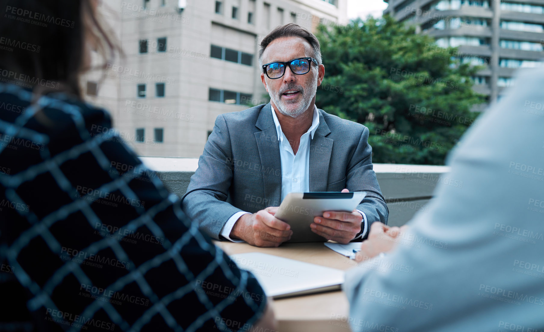 Buy stock photo Shot of a mature businessman using a digital tablet during a meeting with his colleagues on the balcony of an office