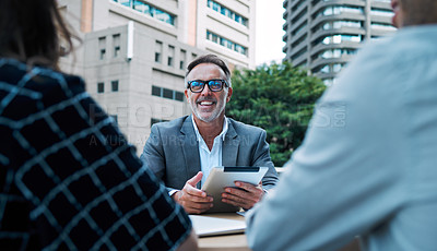 Buy stock photo Shot of a mature businessman using a digital tablet during a meeting with his colleagues on the balcony of an office