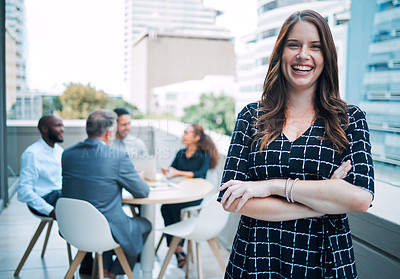 Buy stock photo Portrait of a confident young businesswoman standing on the balcony of an office with her colleagues in the background