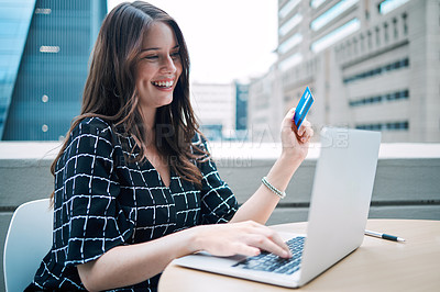 Buy stock photo Shot of a young businesswoman using a laptop and credit card while working on the balcony of an office