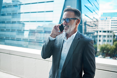Buy stock photo Shot of a mature businessman using a phone in front of a building in the city