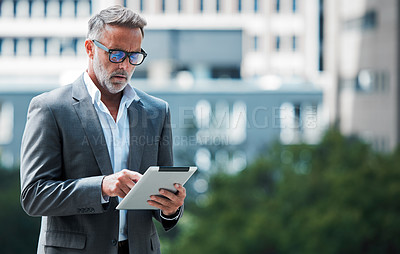 Buy stock photo Shot of a mature businessman using a tablet against an urban background