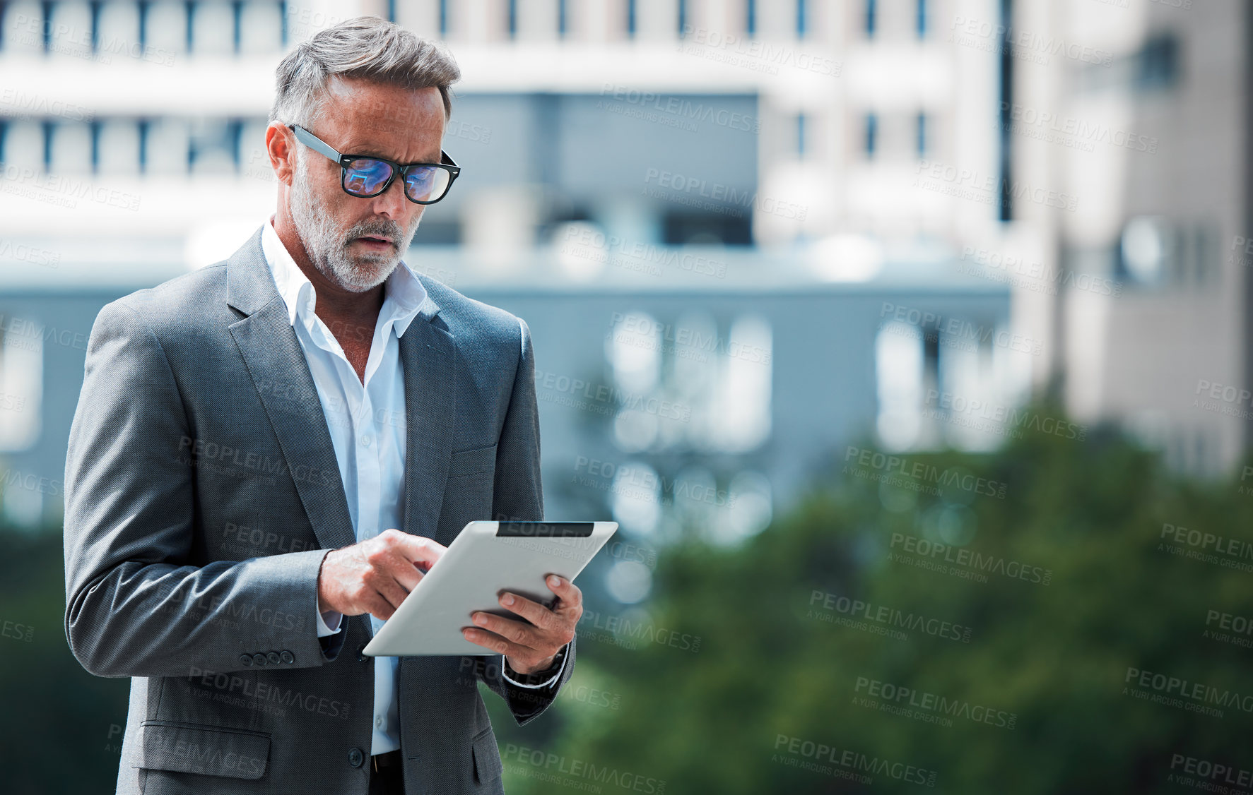 Buy stock photo Shot of a mature businessman using a tablet against an urban background