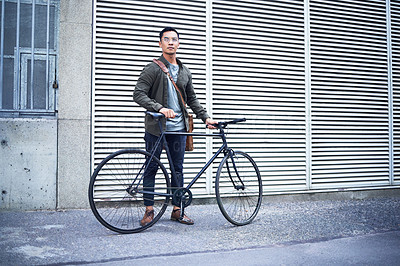 Buy stock photo Shot of a young man posing with a bicycle in the city