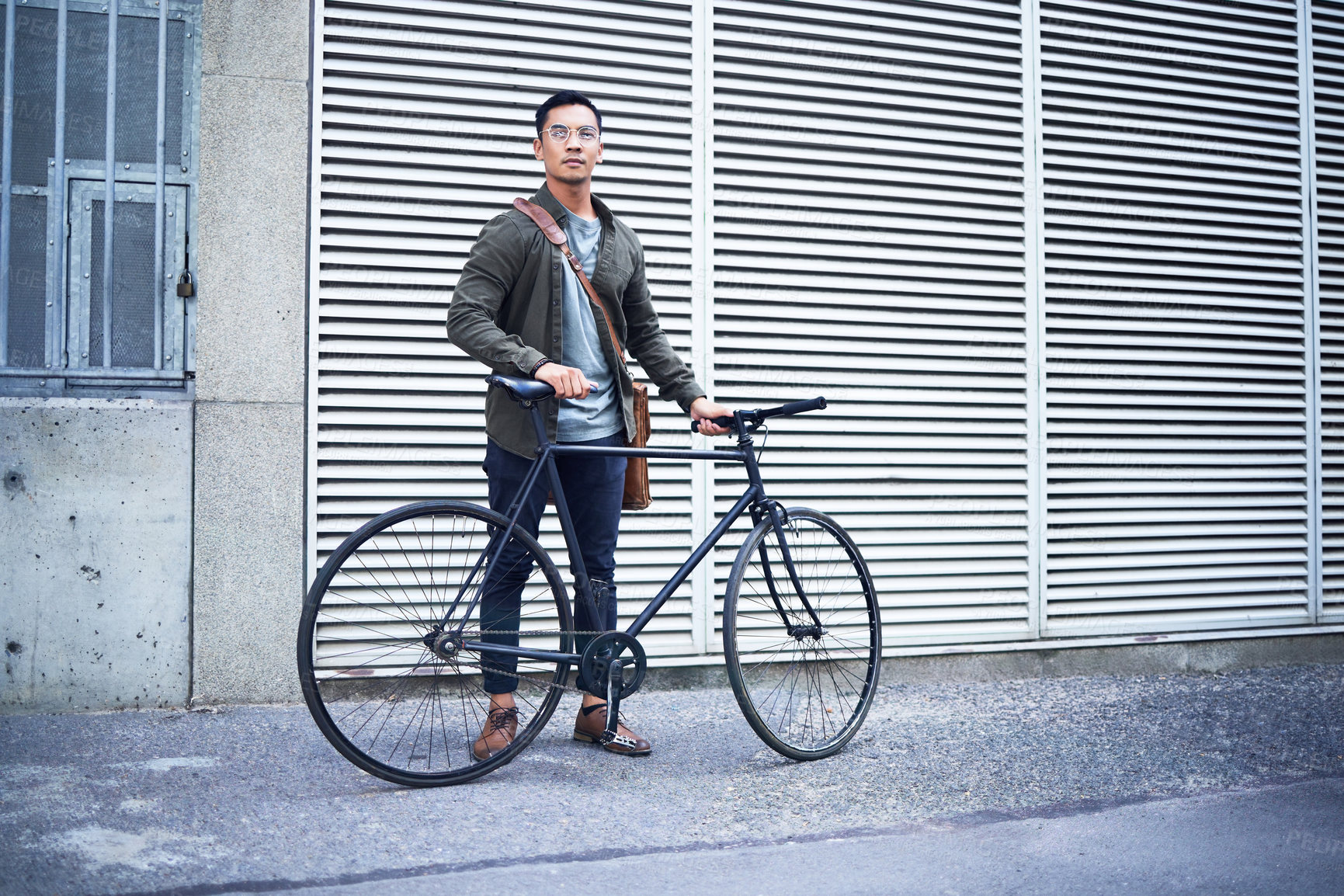 Buy stock photo Shot of a young man posing with a bicycle in the city