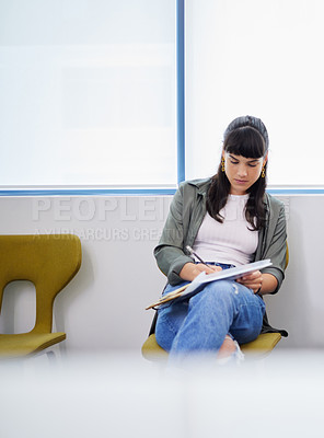 Buy stock photo Shot of a young woman filling in an application for a job at a modern office