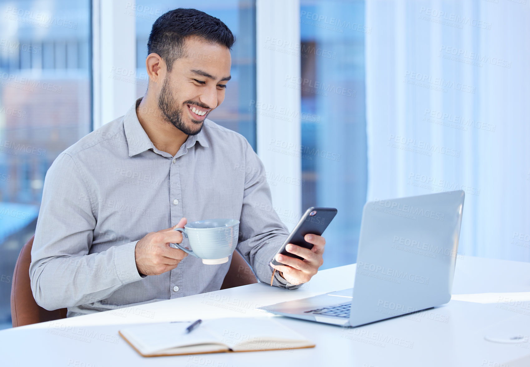 Buy stock photo Shot of a young businessman using his cellphone and drinking coffee while sitting at his desk