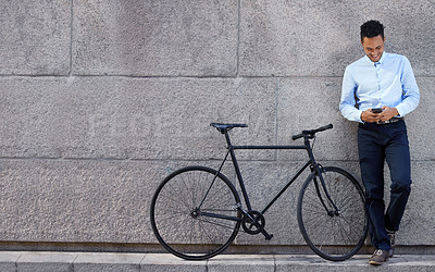 Buy stock photo Full body shot of young businessman standing next to a bicycle while using a cellphone against a grey urban wall