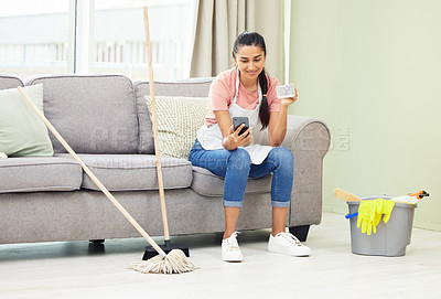 Buy stock photo Shot of a woman using her cellphone and drinking coffee while taking a break from cleaning at home
