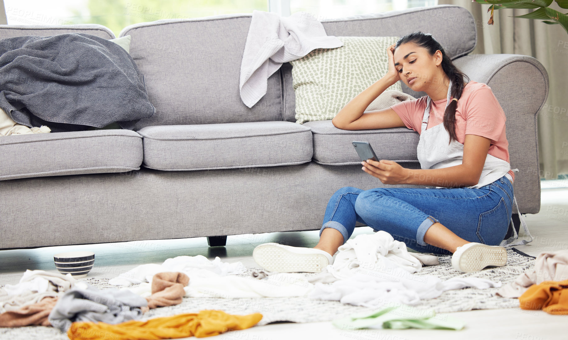 Buy stock photo Shot of a woman sitting on the floor with her cellphone in a messy living room
