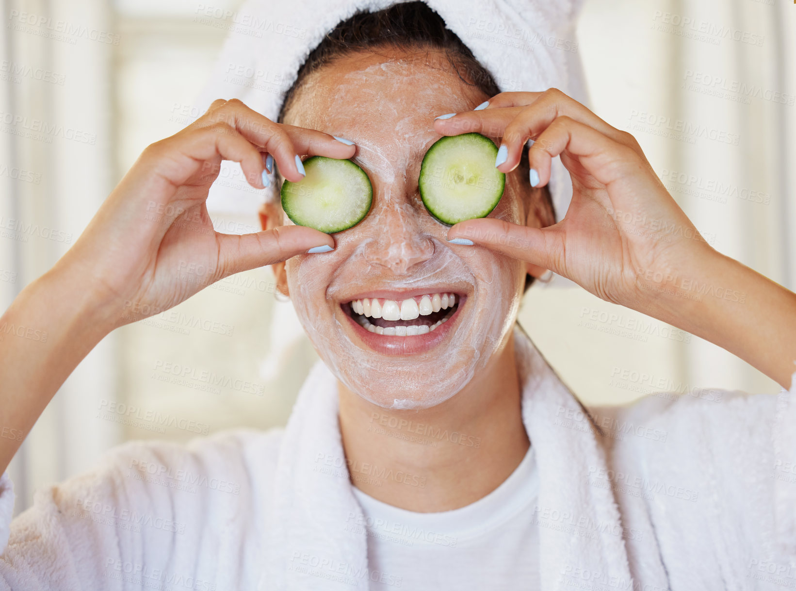 Buy stock photo Shot of a beautiful young woman holding cucumbers in front of her eye during her beauty routine