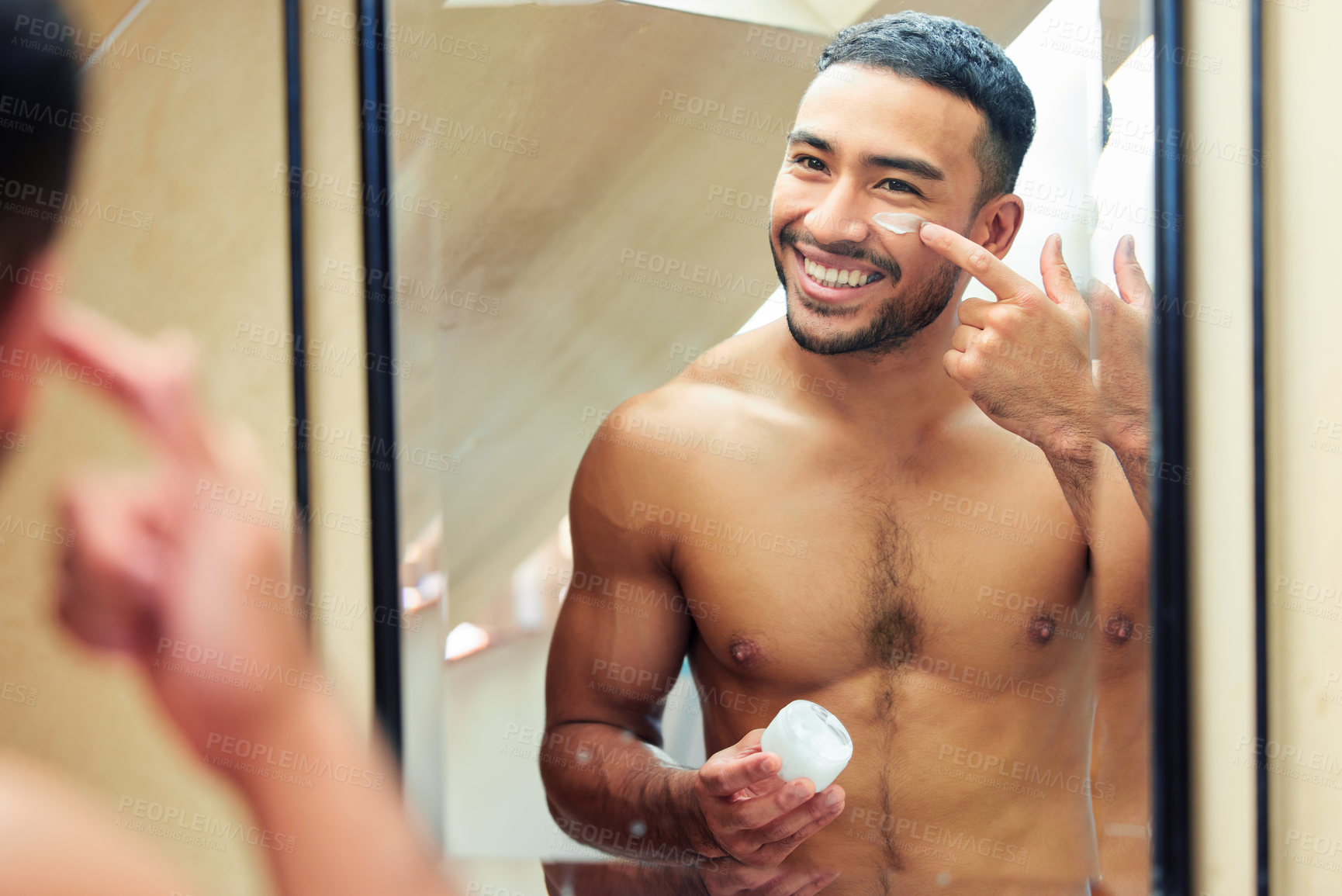 Buy stock photo Shot of a handsome young man looking in the mirror while applying moisturiser to his face