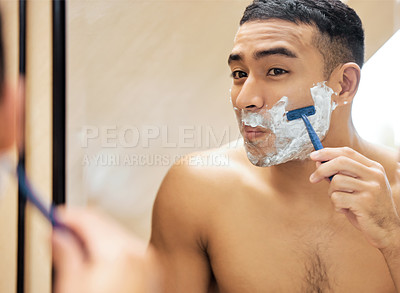 Buy stock photo Shot of a young man looking in the mirror while shaving his beard