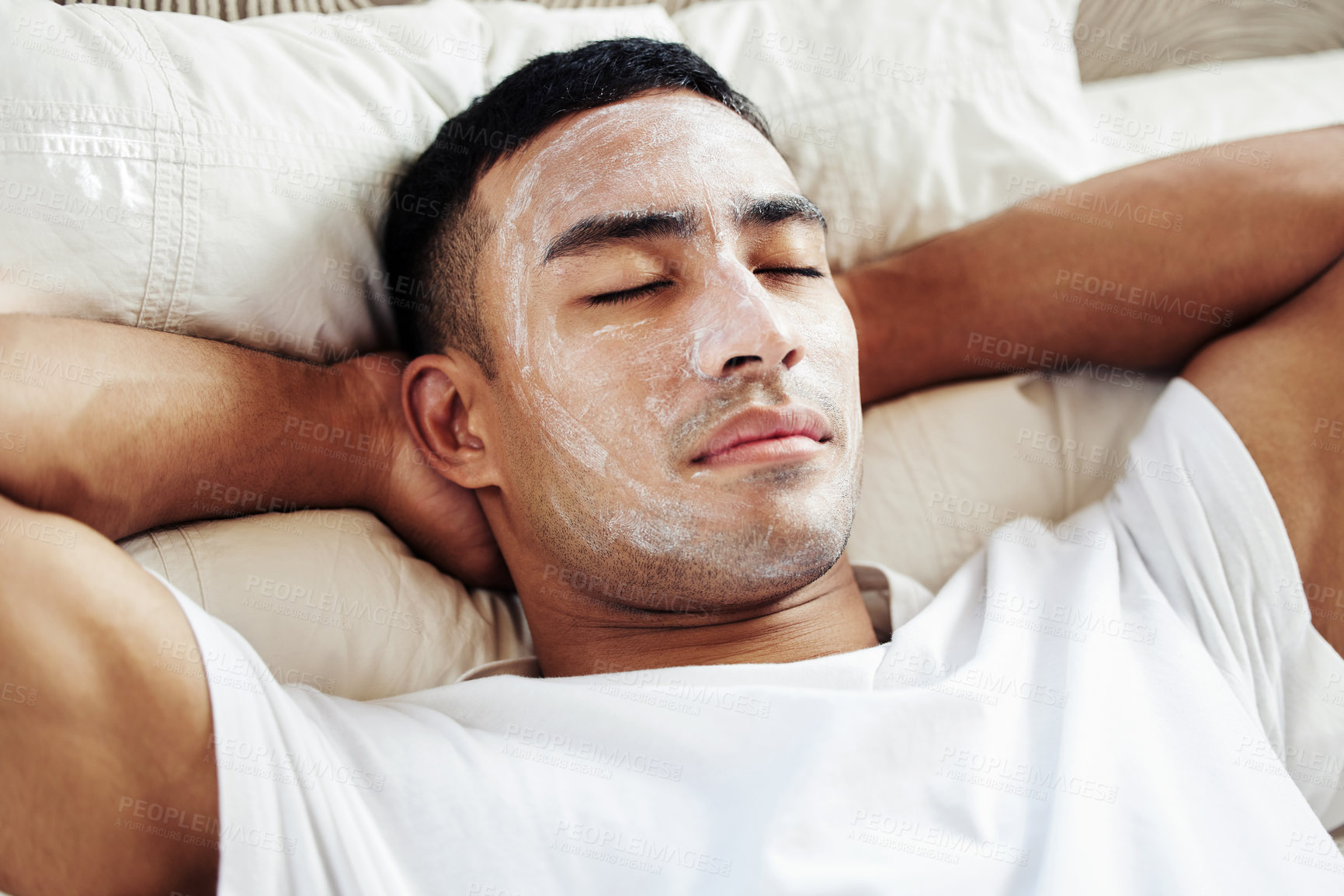 Buy stock photo Shot of a man wearing a cosmetic face mask while lying on his bed at home
